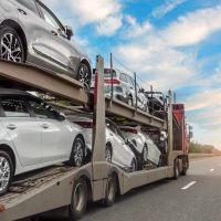 Transportation of new and very expensive cars. Hauling cars trailer and truck pulls rides on the highway. Transport truck hauling cars.