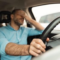 Driver Fatigue. Tired Man Driving Sitting In Car Stuck In Traffic Jam. Male Covering Eyes With Hand Having Problem With Auto While Riding In City. Selective Focus On Steering Wheel