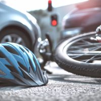 A blue helmet and bicycle lie on the road following a collision with a car, marking the impact of the accident amidst a backdrop of suburban life.