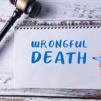 Hand Writing “Wrongful Death” in a Notebook Next to a Gavel, Symbolizing Legal Claim, Tort Law, and Compensation Case