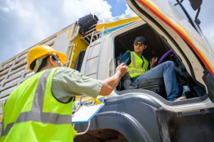 A logistics worker in safety gear hands over documents to a truck driver from outside the vehicle, symbolizing coordination and teamwork in transportation and logistics.
