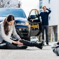 a-woman-sits-on-the-road-holding-her-injured-leg-near-a-fallen-bicycle-and-helmet