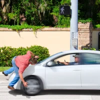 pedestrian-in-a-red-shirt-jumps-onto-a-white-sedans-hood-at-a-crosswalk