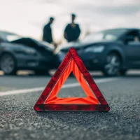 red-warning-triangle-on-road-with-two-damaged-cars-and-blurred-figures-in-the-background